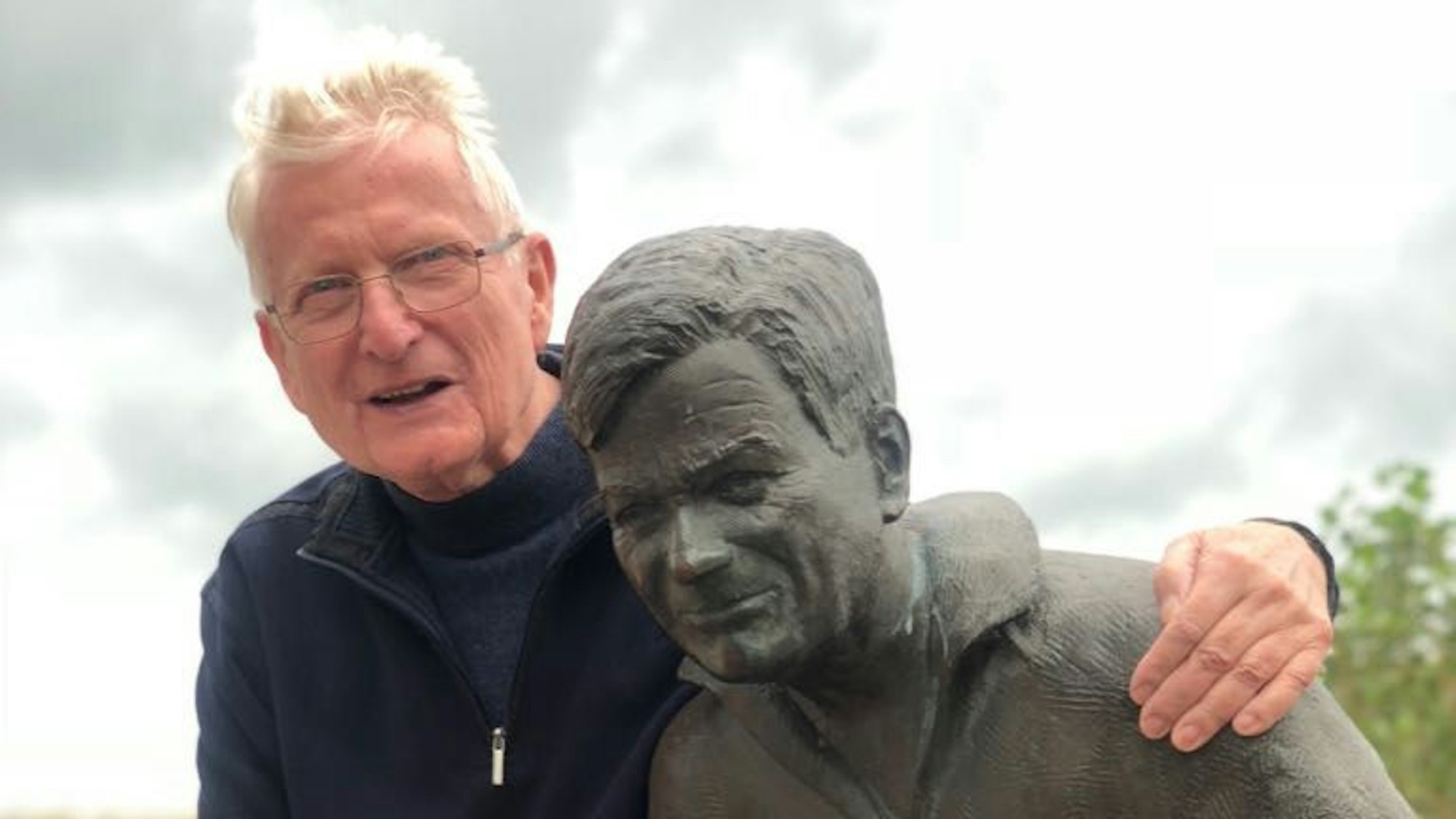 Franz Kersjes umarmt eine Statue und lächelt in die Kamera.