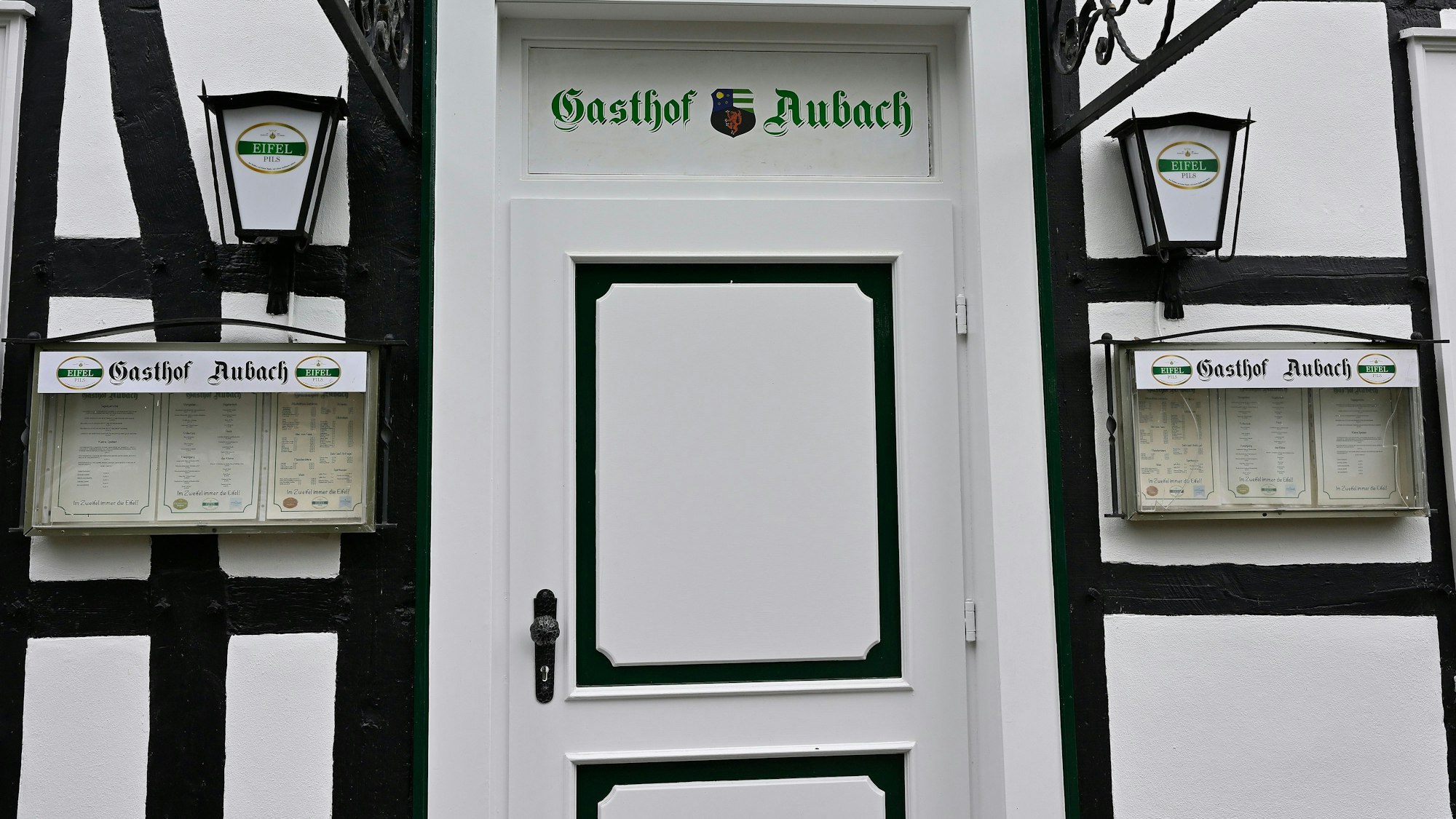 Neben einer Tür über der der Gaststättenname „Gasthof Aubach“ zu lesen ist, hängen Speisekarten an der Wand eines Fachwerkhauses.
