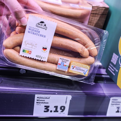 Zwei Preisschilder hängen im Kühlregal vor einer Packung mit Wiener Würstchen.