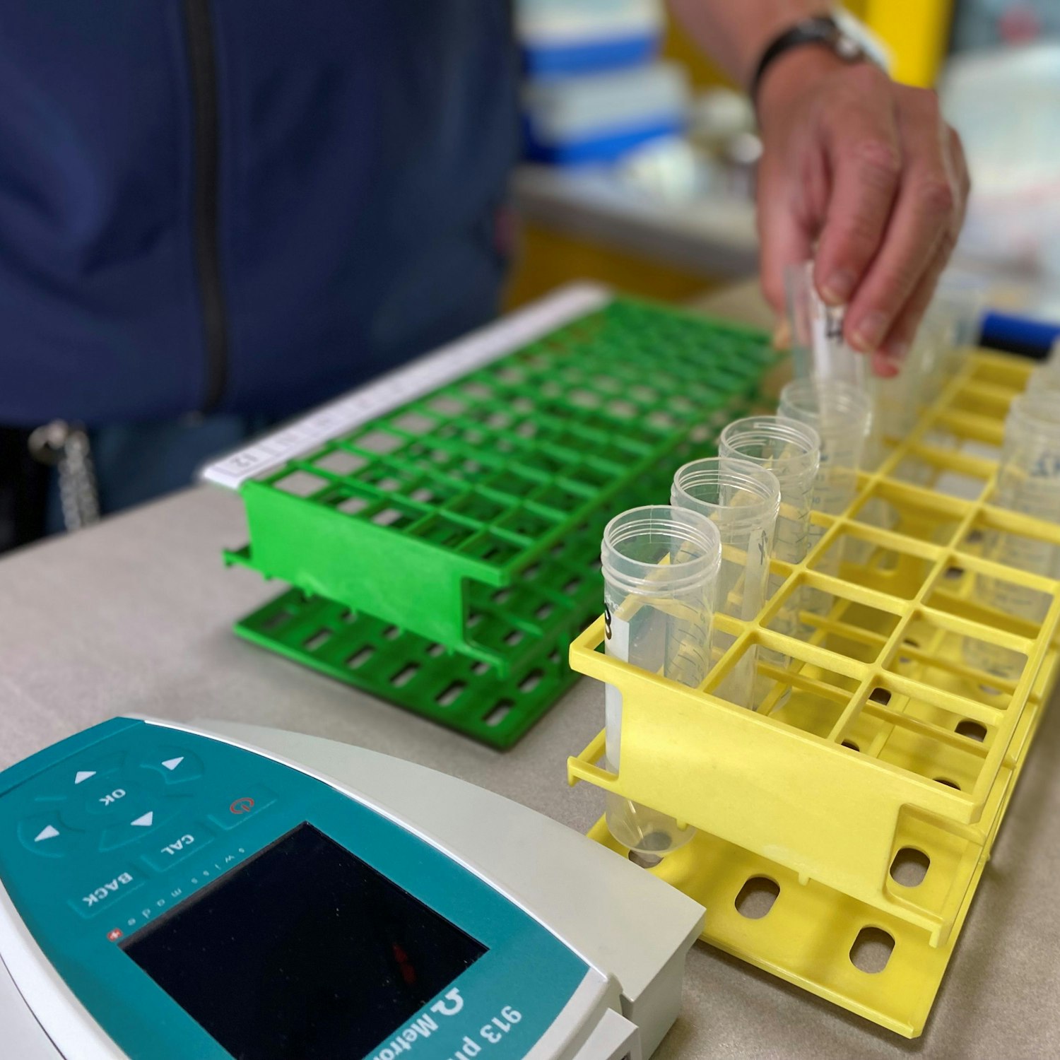 Reagenzgläser aus Plastik und ein pH-Messgerät liegen auf einem Tisch.