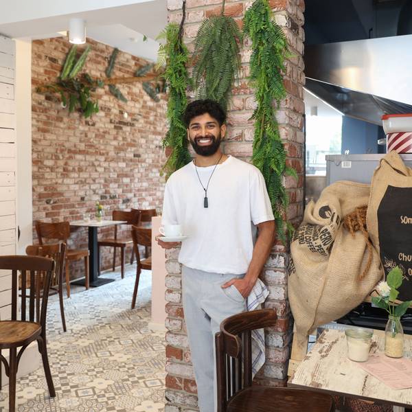 Kassim Hussain steht an einer Säule und hält eine Tasse Kaffee.