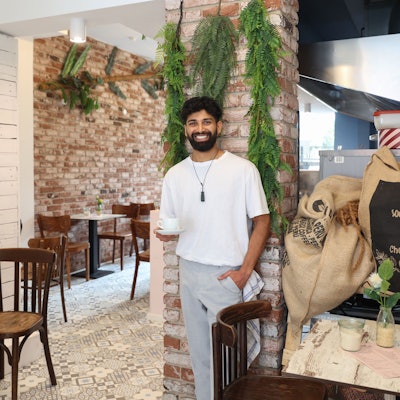 Kassim Hussain steht an einer Säule und hält eine Tasse Kaffee.