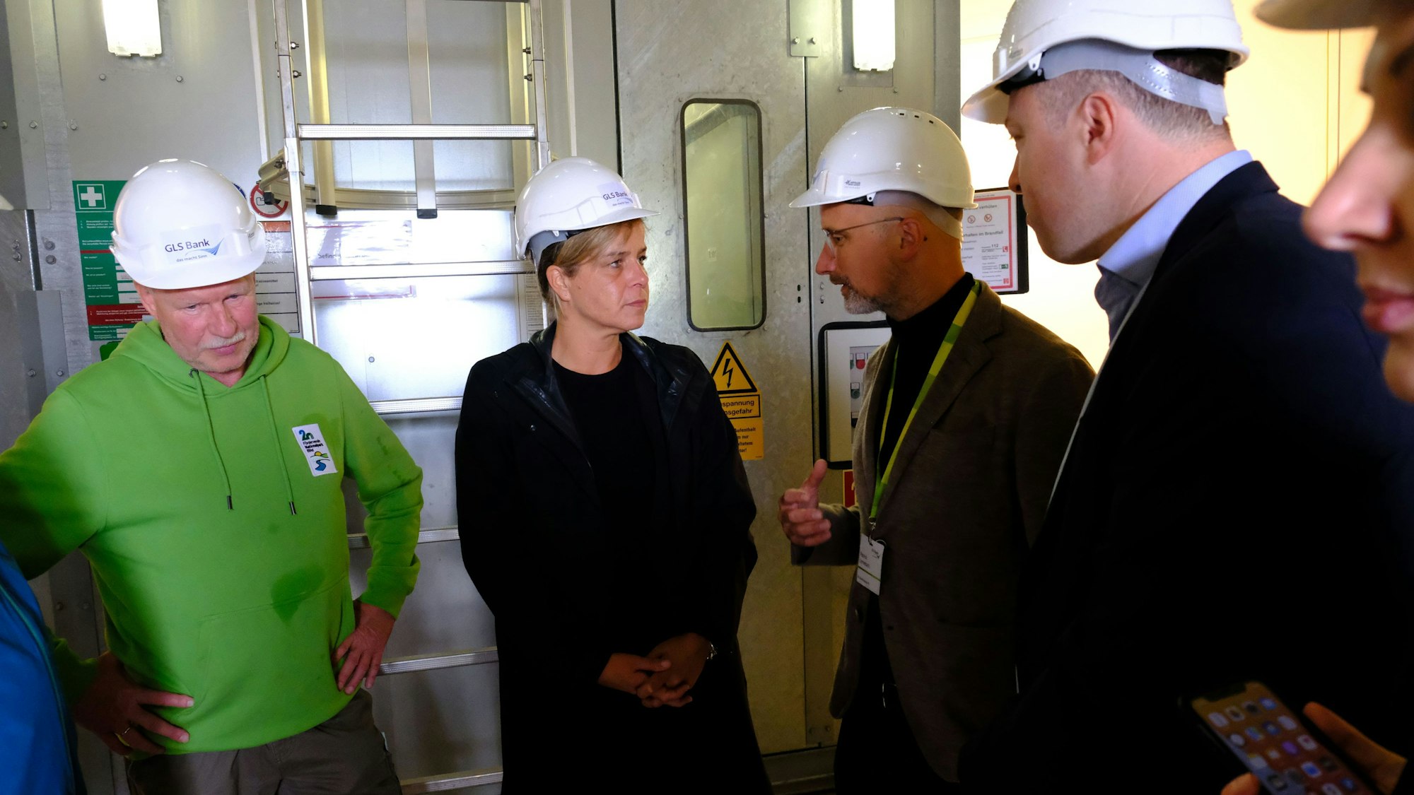 Eine Frau und drei Männer stehen im Inneren eines Windrades. Sie tragen weiße Schutzhelme.