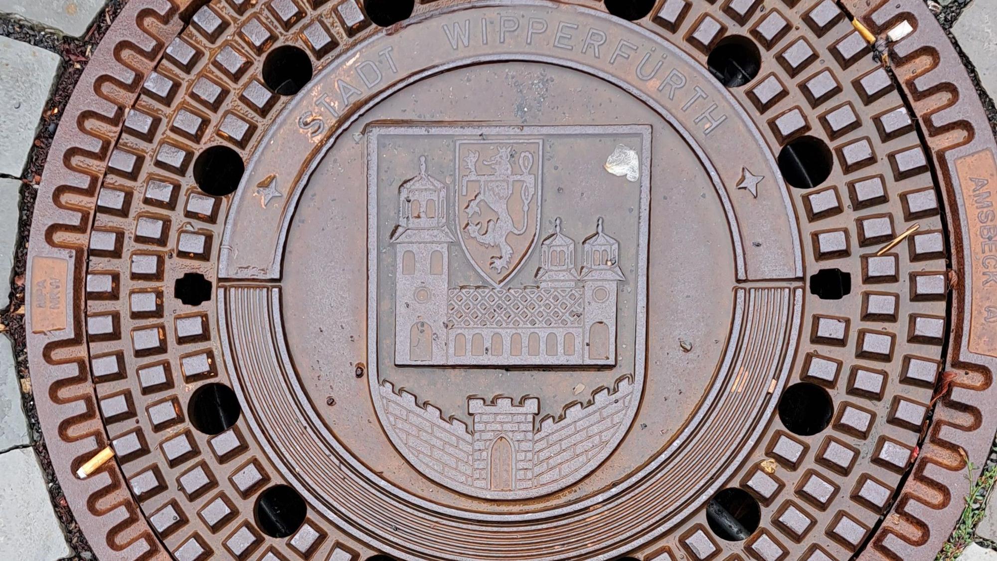 Das Bild zeigt einen Kanaldeckel mit dem Wipperfürther Stadtwappen und dem Schriftzug „Stadt Wipperfürth“.