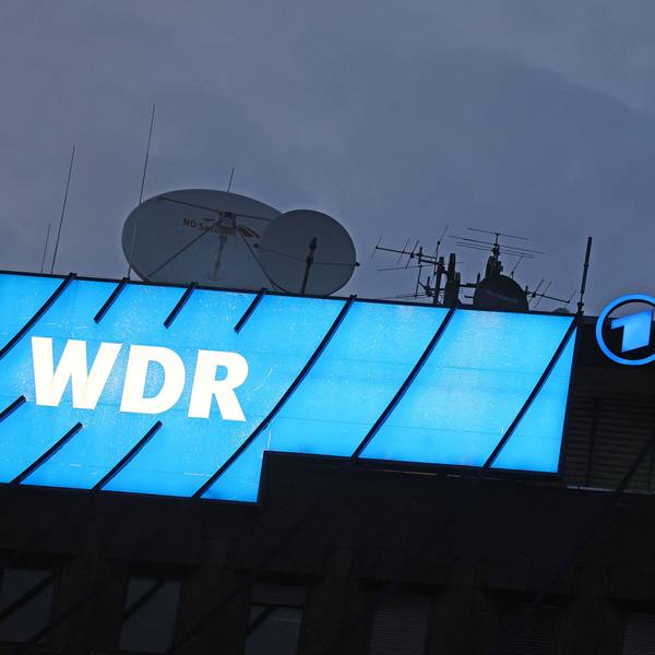 Das Logo des Nachrichtensenders WDR leuchtet auf dem Dach des WDR-Gebäudes in der Kölner Innenstadt.