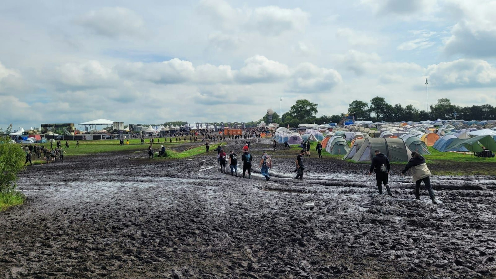 Besuchende des Wacken-Festivals bahnen sich unter Schwierigkeiten ihren Weg durch den Schlamm zur Bühne.