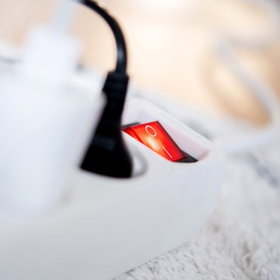 Die Netzstecker verschiedener Elektrogeräte stecken in einer Steckdosenleiste in einem Wohnzimmer.