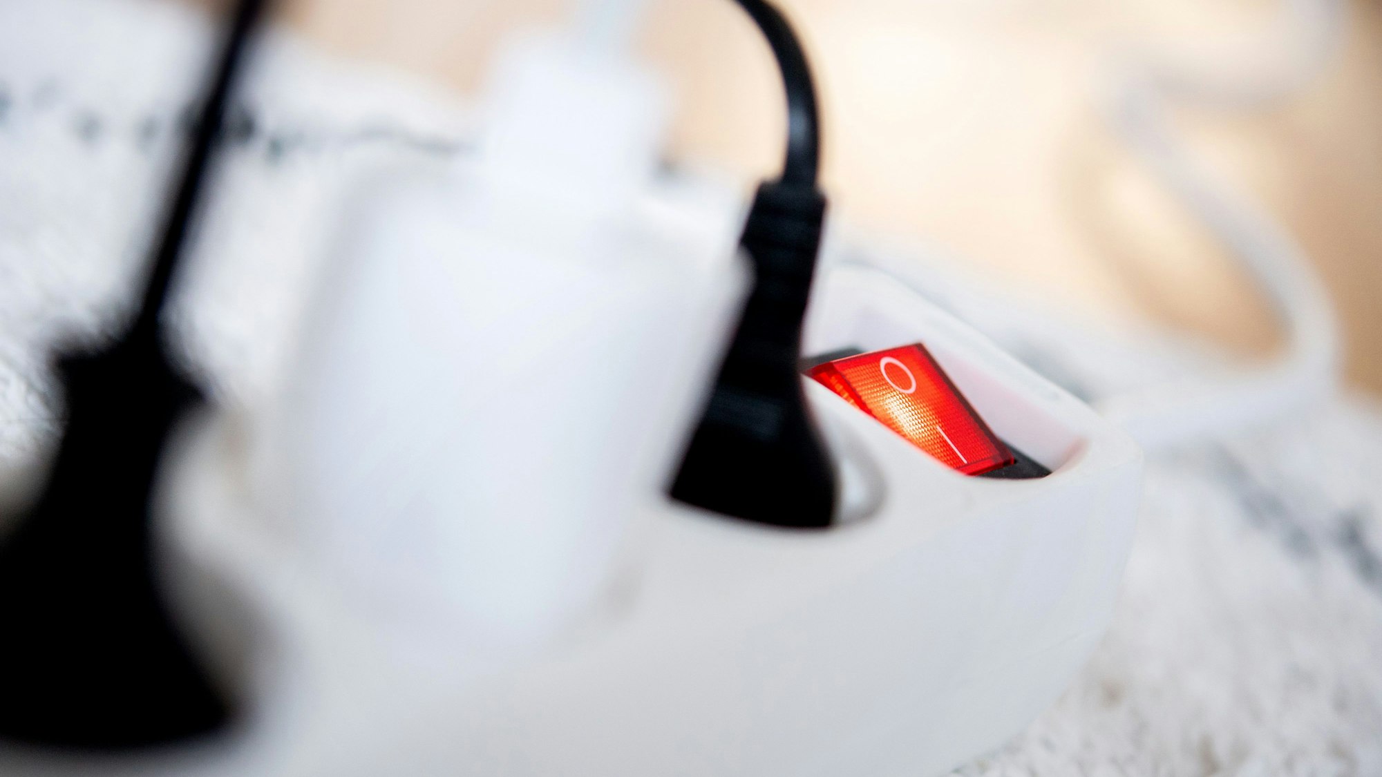 Die Netzstecker verschiedener Elektrogeräte stecken in einer Steckdosenleiste in einem Wohnzimmer.