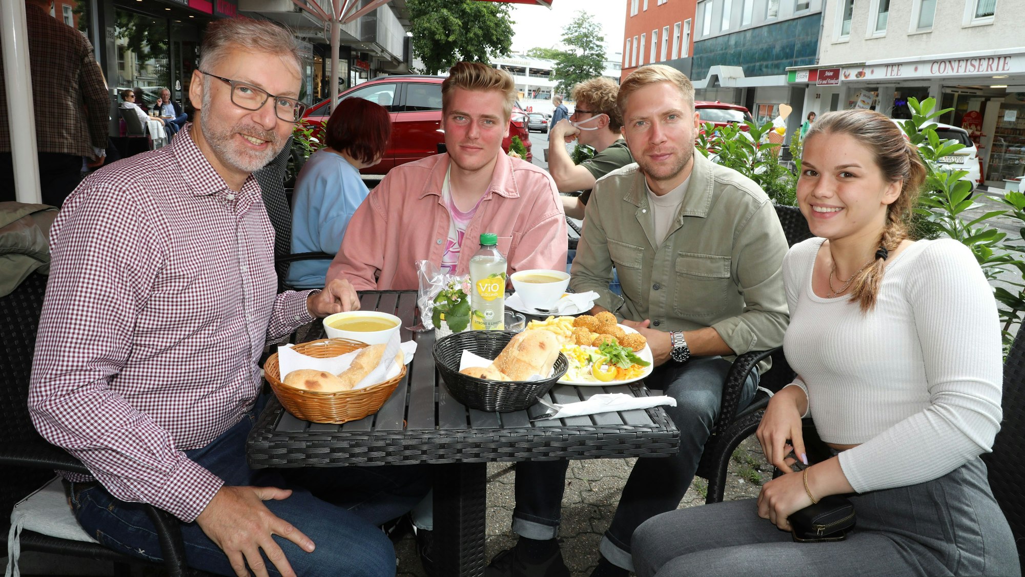 Dr. Oliver Schillings und seine Mitarbeitenden Lukas Litzka, Adrian van Heerd und Pauline Quiring sitzen an einem Tisch der Außengastronomie des Schlossgrills in der Bensberger Schloßstraße.