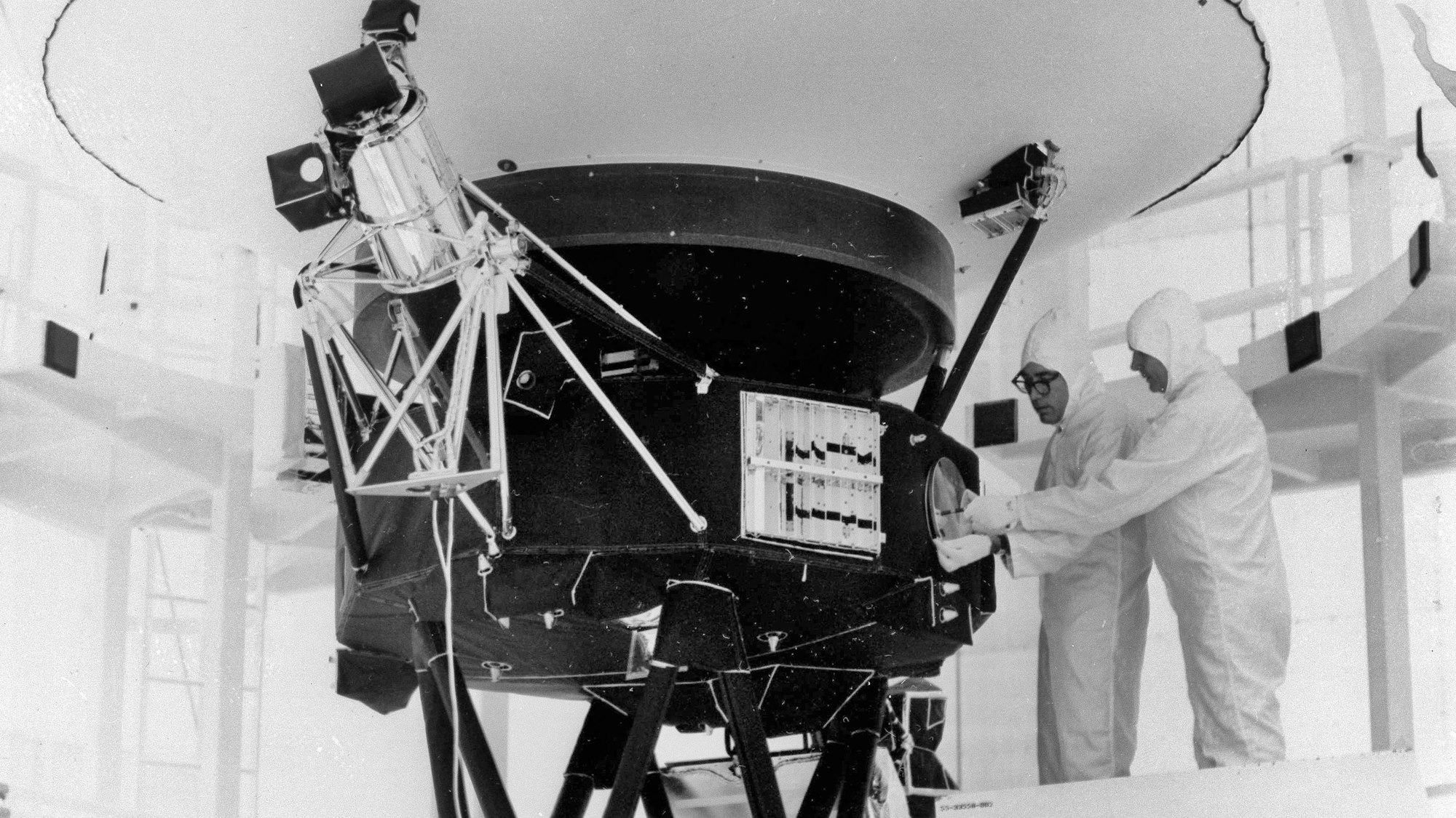 Mehrere Wissenschaftler der US-Weltraumbehörde Nasa arbeiten kurz vor dem Start an der Fertigstellung der weltberühmten Raumsonde Voyager 2. Sie tragen weiße Anzüge.