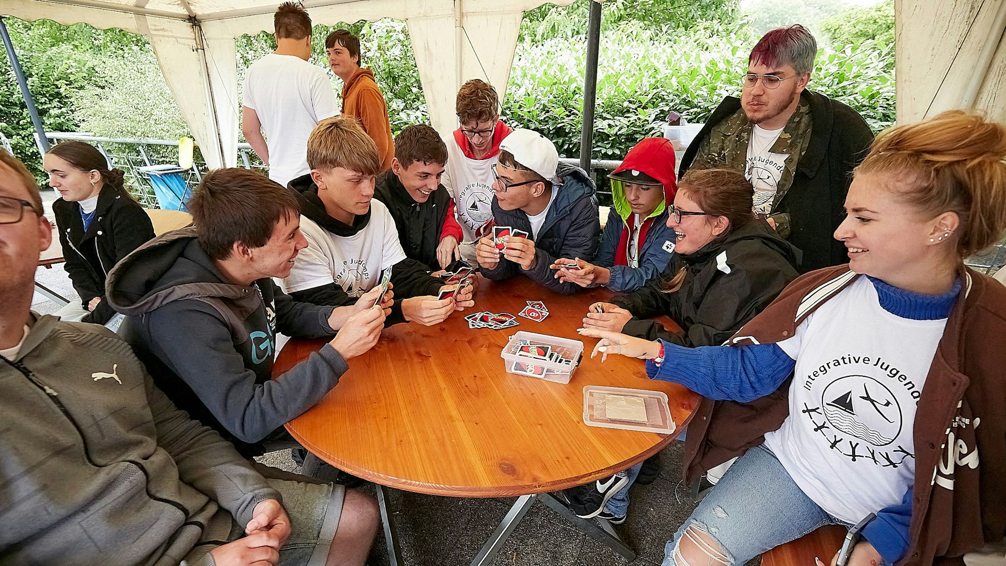 Um einen runden Tisch sitzen viele jugendliche Teilnehmer des Segelcamps und spielen das Kartenspiel Uno.