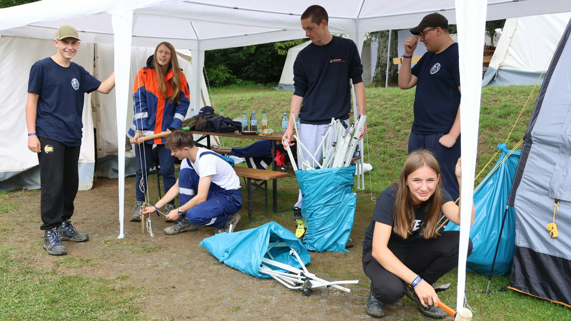 Mehrere junge Menschen bauen auf einem Zeltplatz einen Pavillon auf.