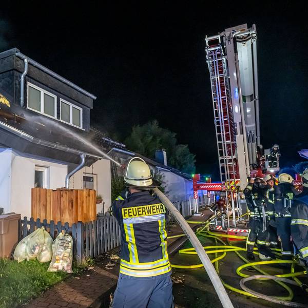 Ein Feuerwehrmann hält einen Schlauch, aus dem ein Wasserstrahl kommt, in Richtung eines brennenden Dachstuhls.