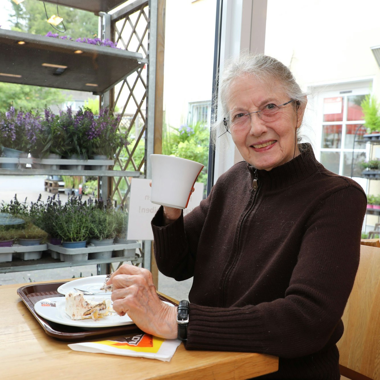 Carla Weidemeyer sitz mit einer Tasse Kaffee und einem Stück Kuchen auf einem Teller im Café der Bäckerei Lob im Odenthaler Rewe-Markt.