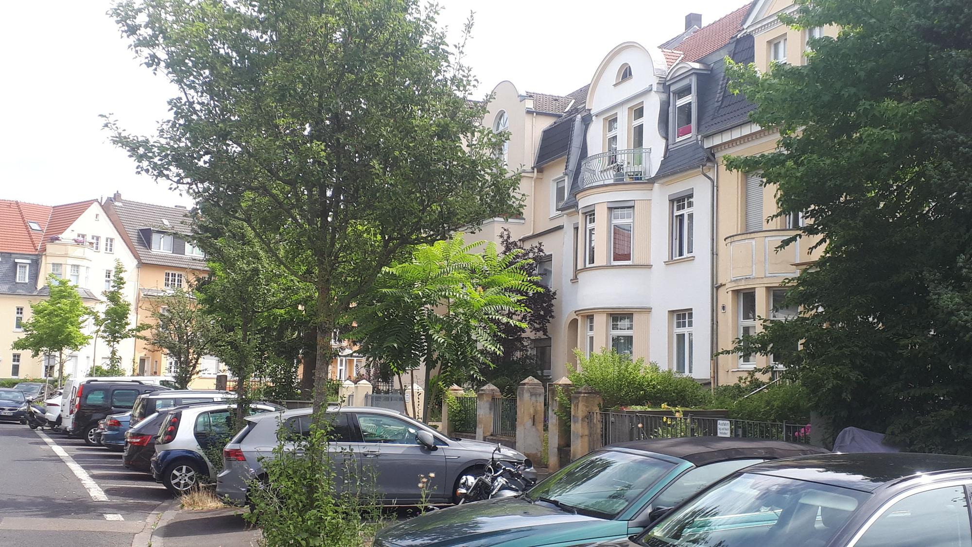 An einer Straße stehen Altbauvillen nebeneinander, davor parken Autos.