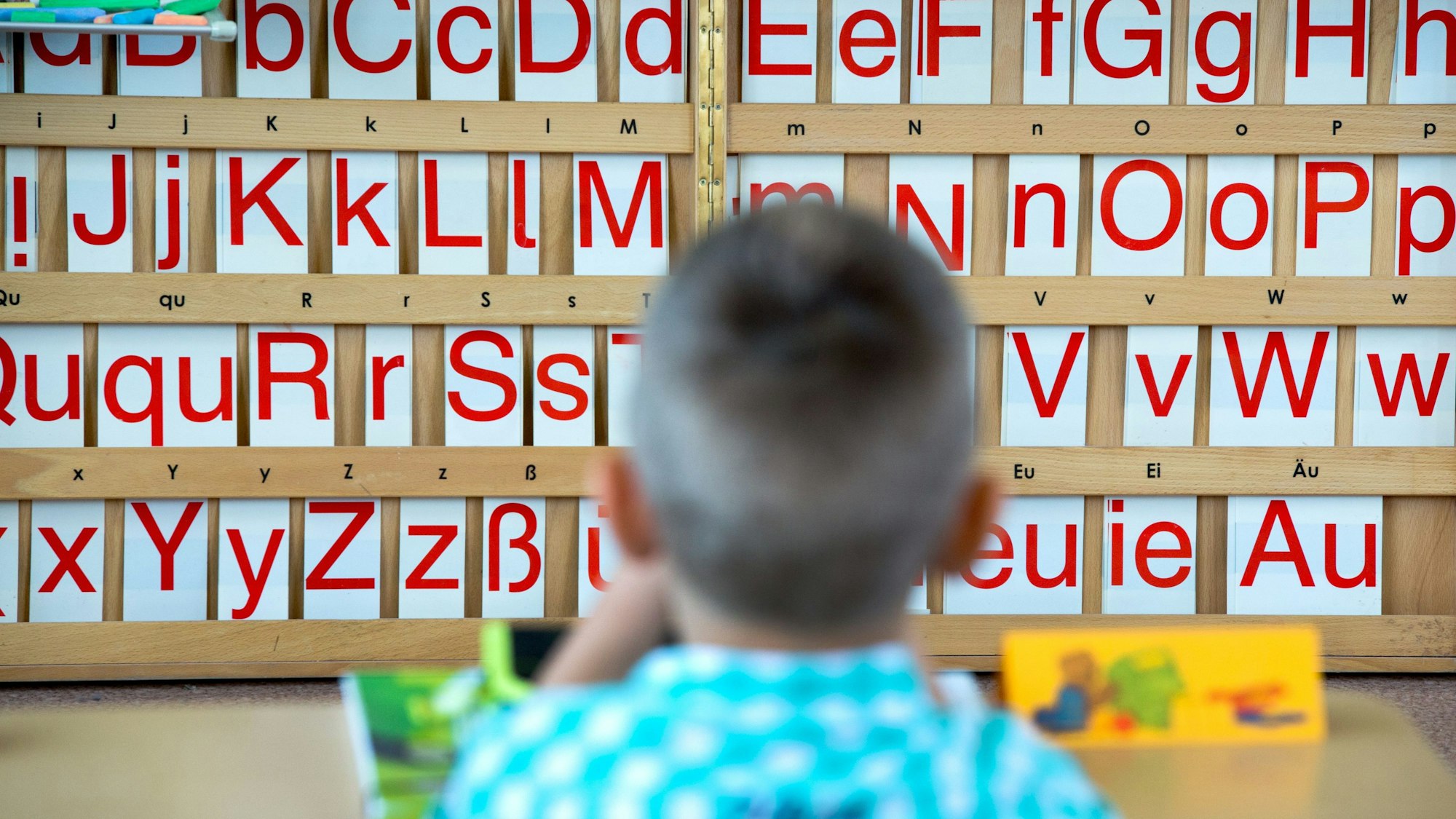 Ein Erklässler sitzt vor einer Buchstabentafel.