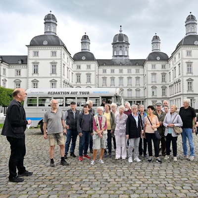 Eine Gruppe und ein  historischer Bus stehen im Innenhof von Schloss Bensberg.