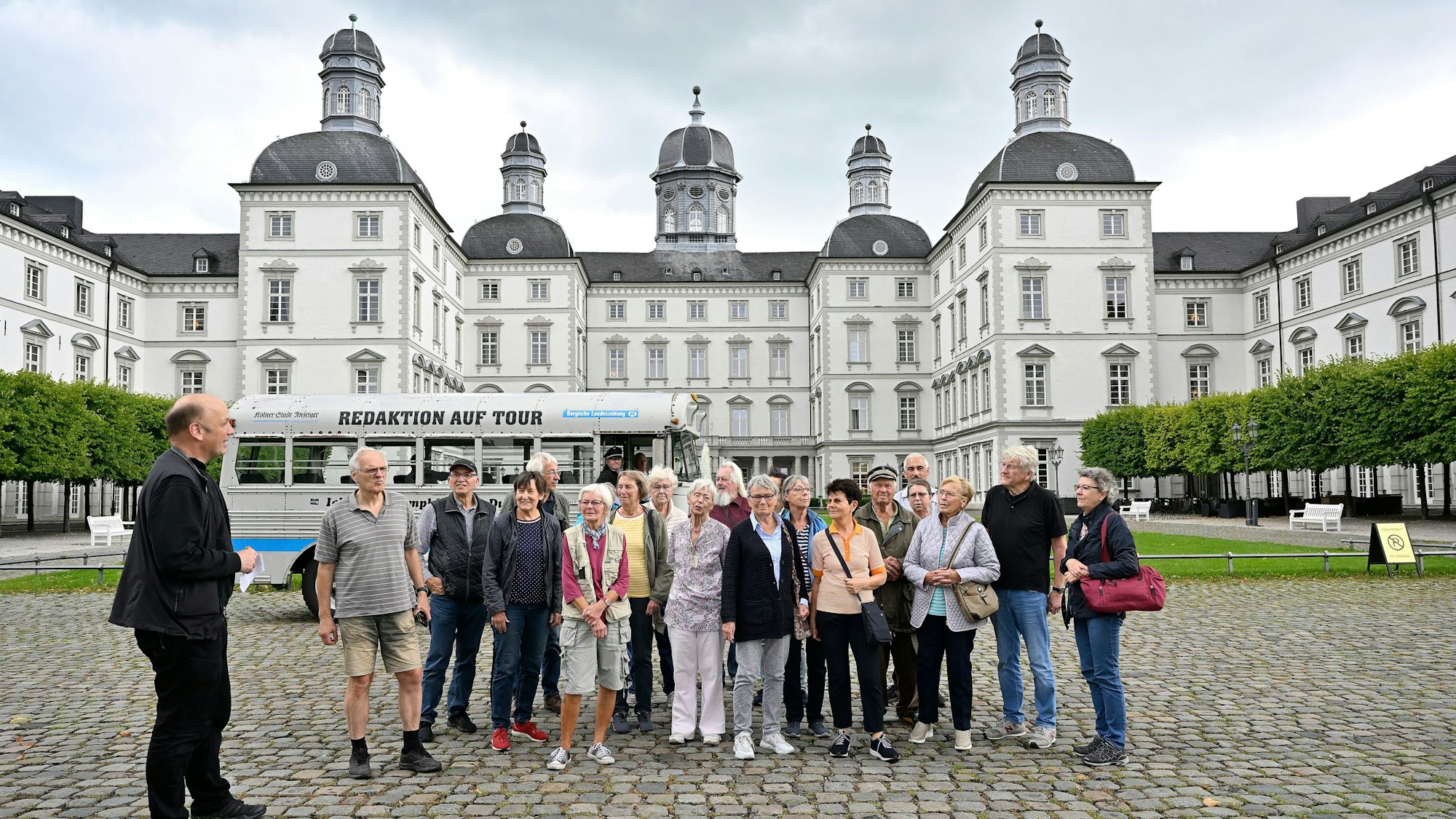 Eine Gruppe und ein  historischer Bus stehen im Innenhof von Schloss Bensberg.