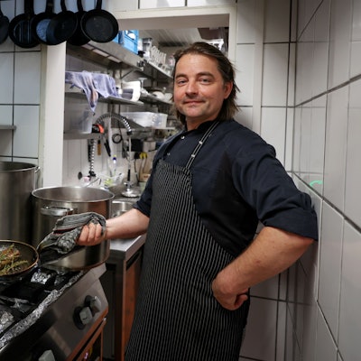David Safanda vom Crevette Rosé steht in der Küche und brät ein Stück Fleisch in der Pfanne.