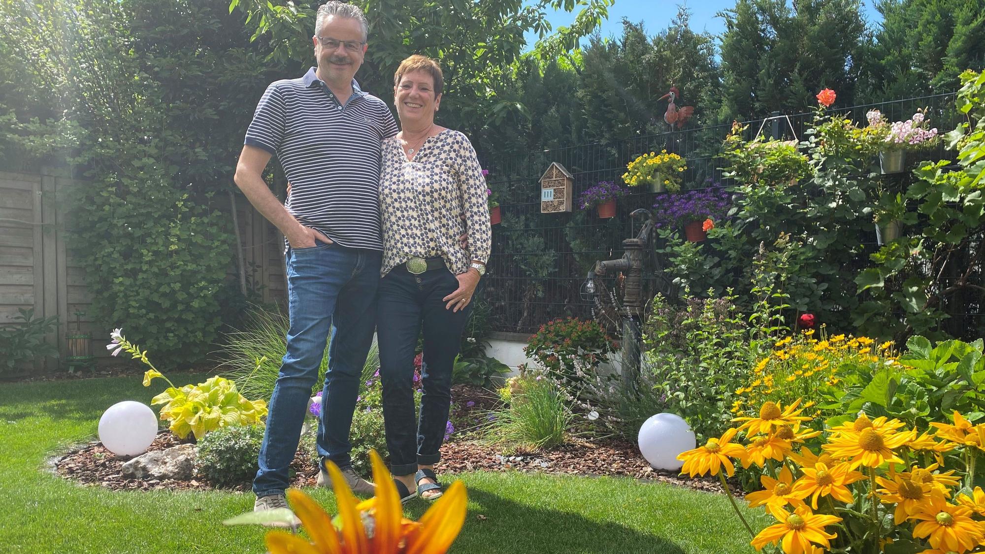 Addi Kirfel und Marion Selbst stehen inmitten ihres gut bewässerten und blühenden Gartens.
