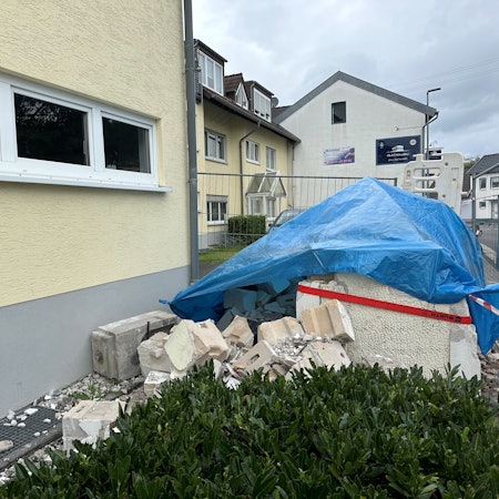 Ein Haufen Schutt liegt vor einem Haus. Er ist mit einer blauen Plane bedeckt.