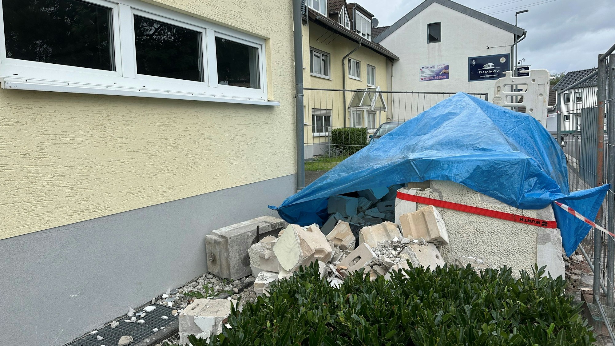 Ein Haufen Schutt liegt vor einem Haus. Er ist mit einer blauen Plane bedeckt.