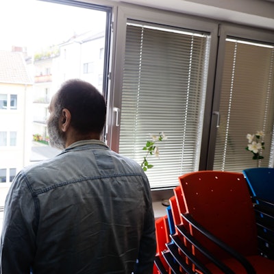 Langzeit-Cannabis-Konsument steht am Fenster eines Raums der Drogenhilfe Köln, Rückenansicht.