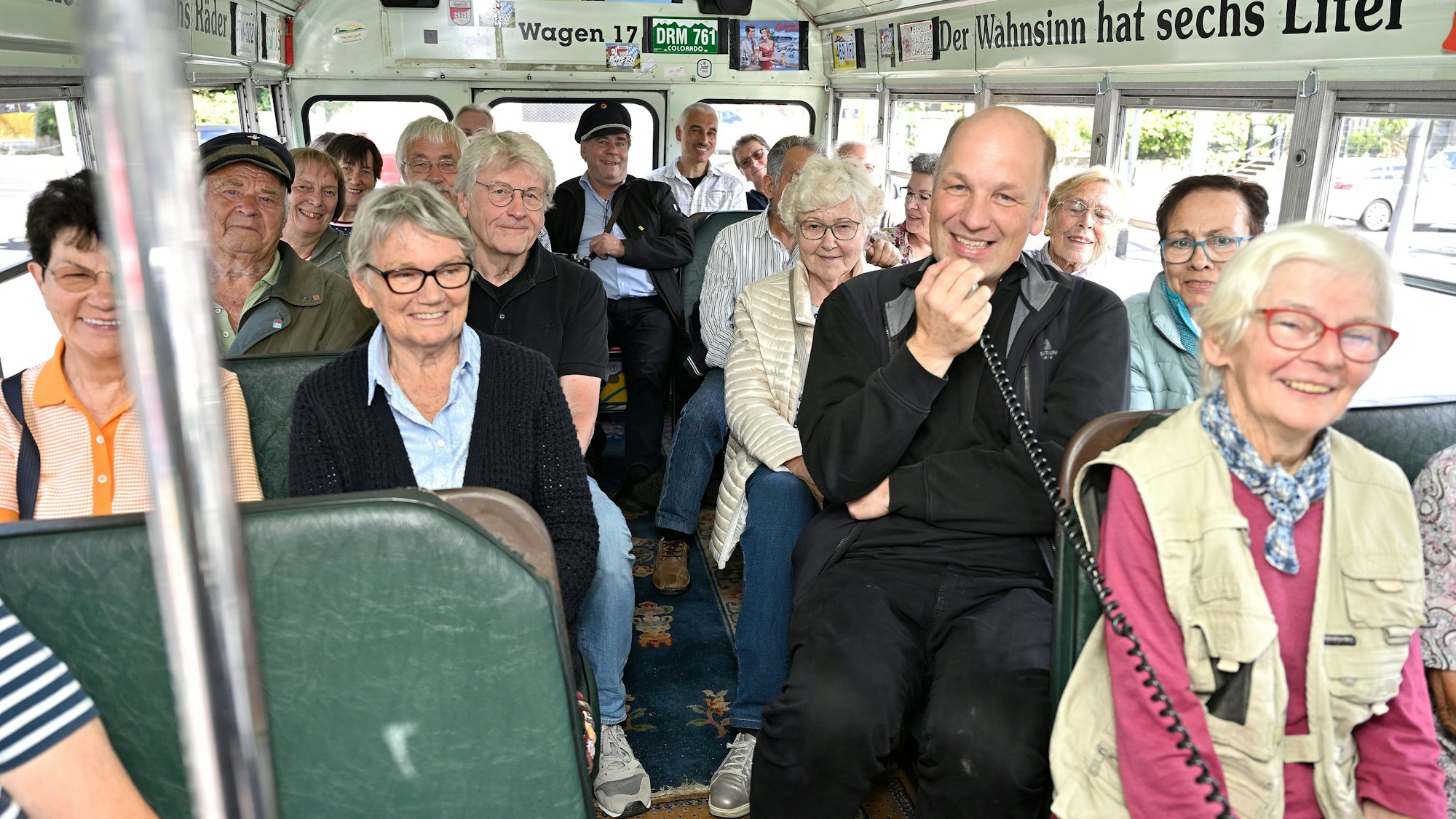 in einem historischen  amerikanischen  Schulbus sitzen Menschen, einer von ihnen spricht offenkundig in ein Mikrofon.