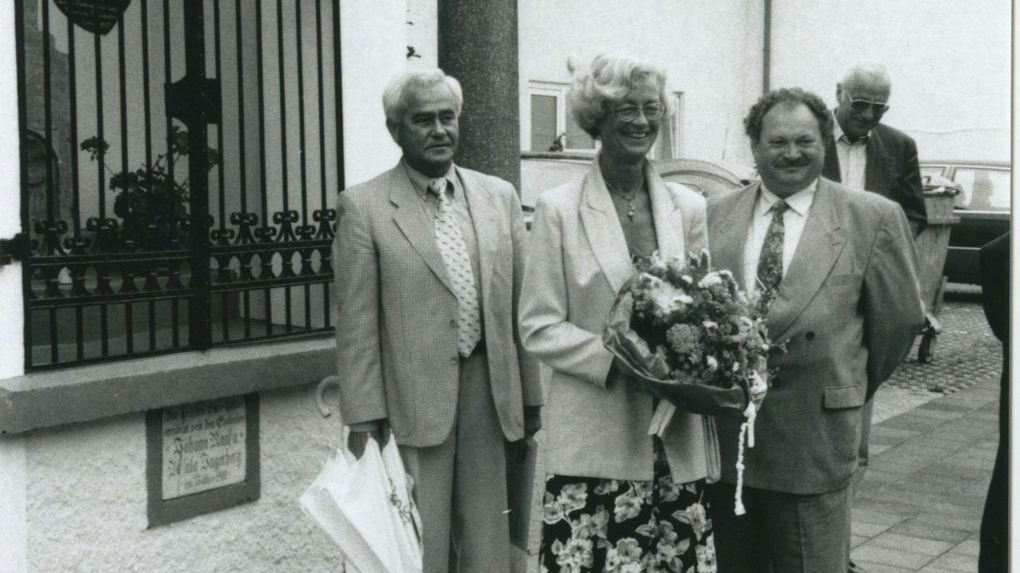 Zwei Männer und eine Frau stehen vor einem Heiligenhäuschen.