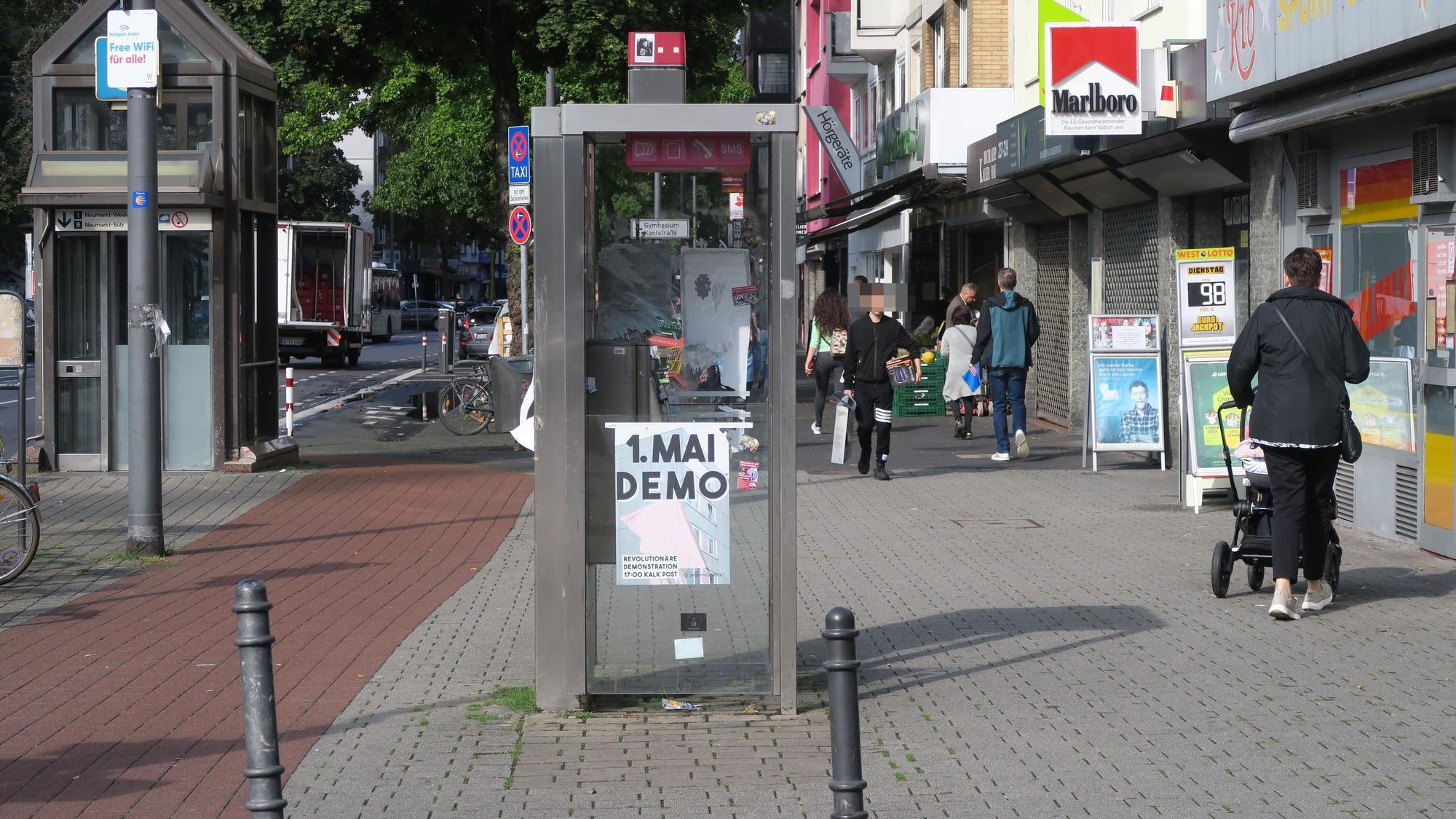 Menschen laufen auf einer Geschäftsstraße an einer leerstehenden Telefonzelle vorbei.