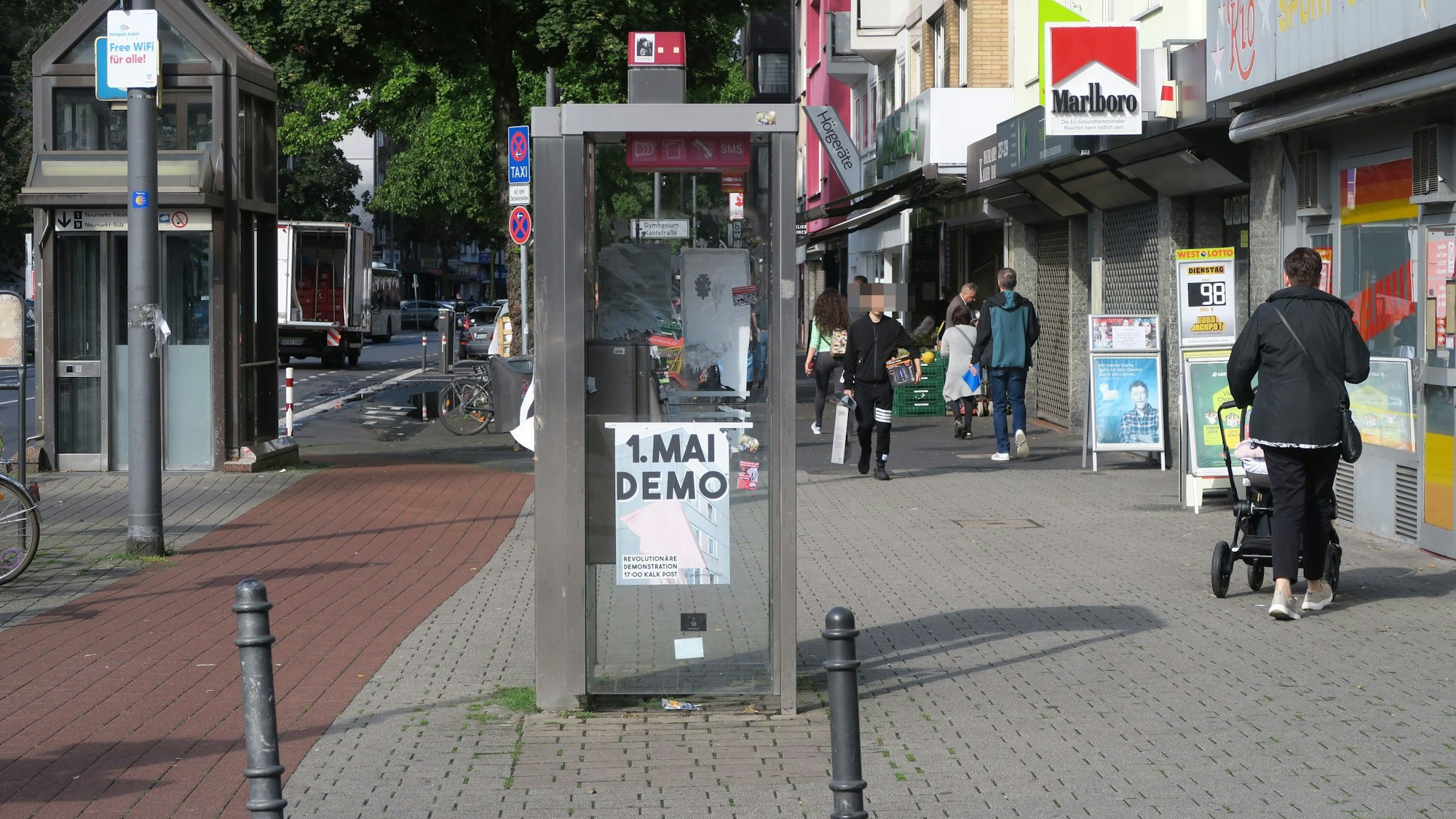 Menschen laufen auf einer Geschäftsstraße an einer leerstehenden Telefonzelle vorbei.
