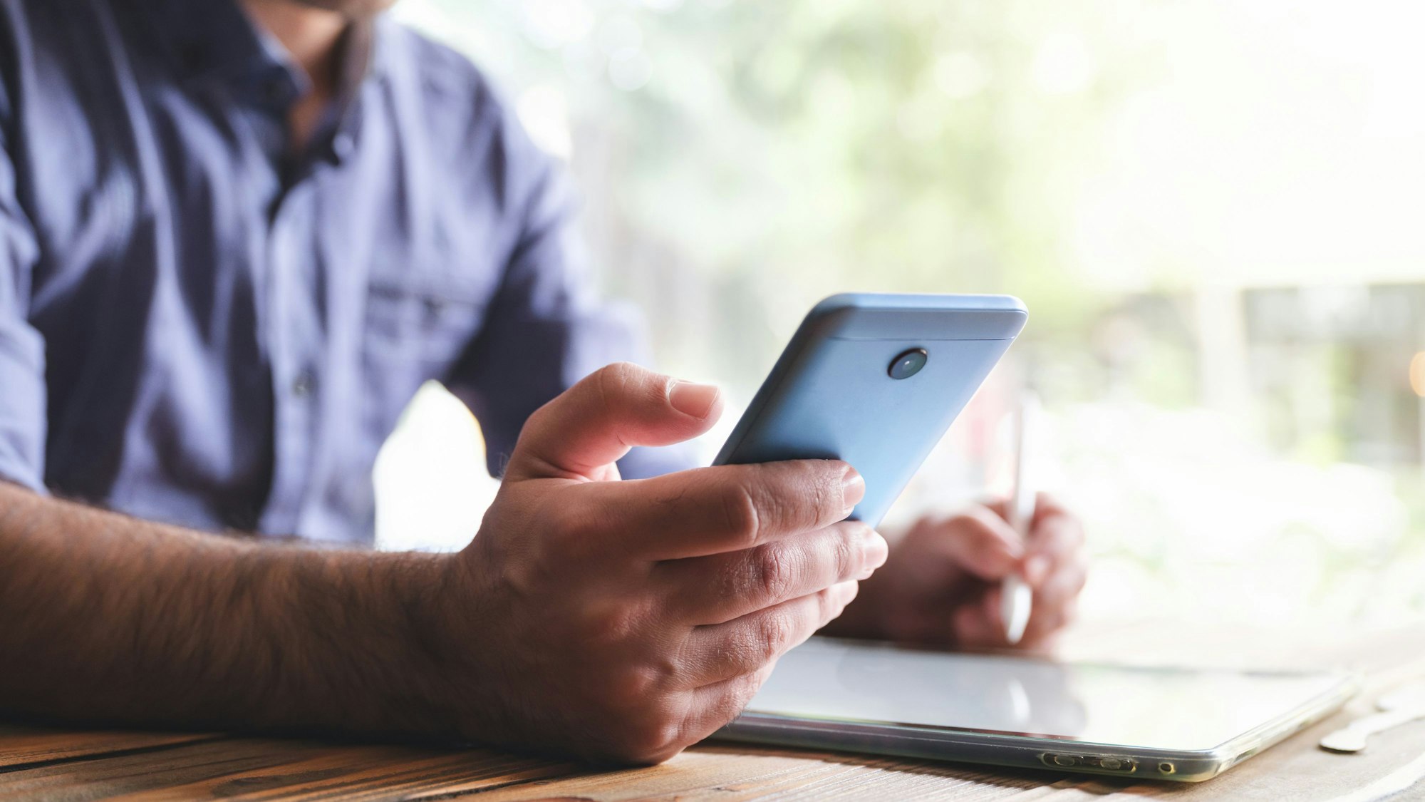 Ein Mann unterschreibt auf einem digitalen Tablet, mit einem Stift und kontrolliert sein Smartphone.