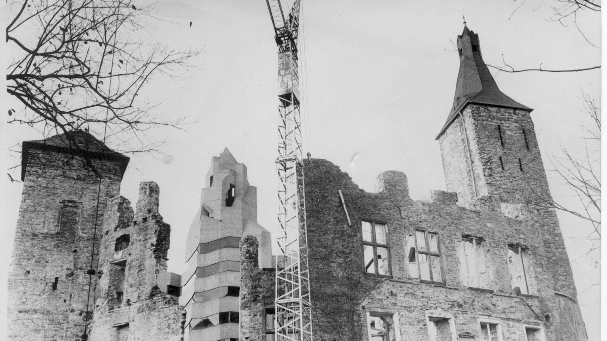 Abbruch eines Teils der Außenmauer des Alten Schlosses im Vordergrund Fassade des Alten Schlosses, rechts und links Türme. Die Mauer ist an einer Stelle durchbrochen. Im Hintergrund fertiggestellter Turm des Rathauses, Aufnahme um 1967