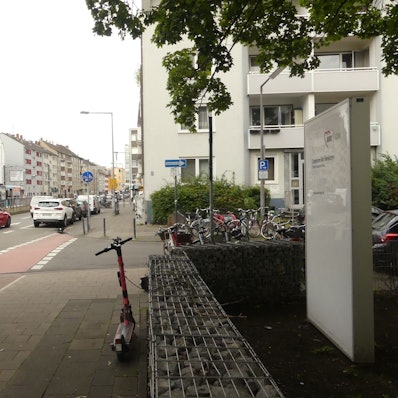 Eine zweispurige Straße mit einer Straßenbahnhaltestelle in der Mitte ist zu sehen. Im Vordergrund steht das Schild der Senioreneinrichtung, die unmittelbar an der Straße liegt.