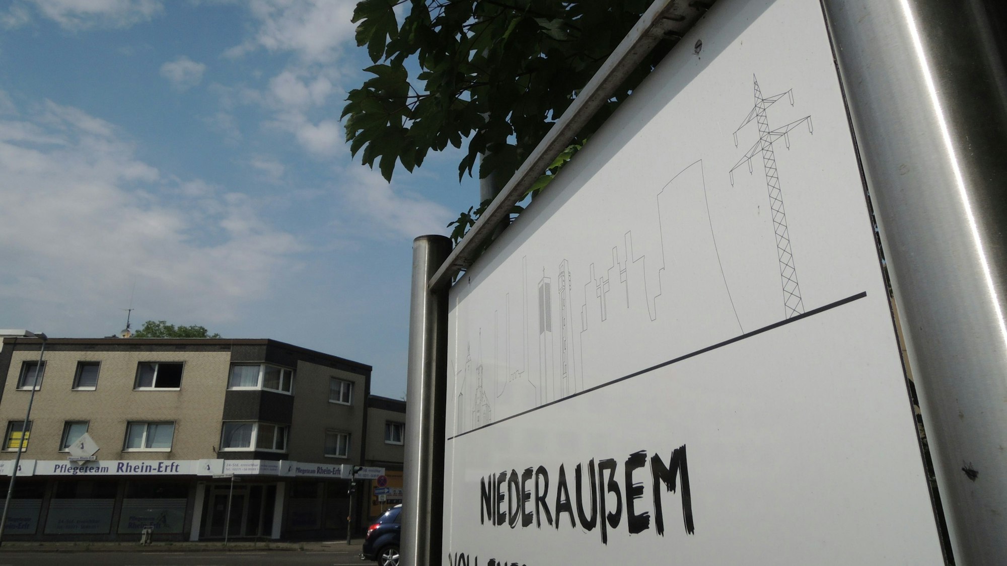 Auf einem Schild aus Metall steht „Niederaußem“, im Hintergrund sind Gebäude.