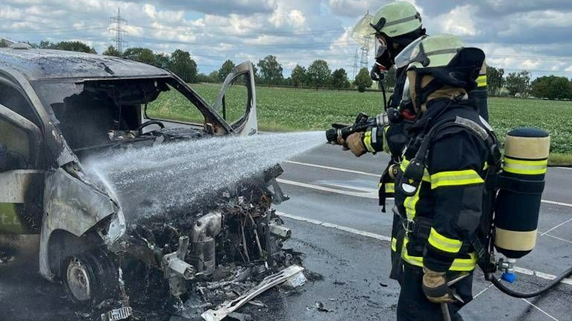 Zwei Einsatzkräfte der Feuerwehr löschen das ausgebrannte Fahrzeug.