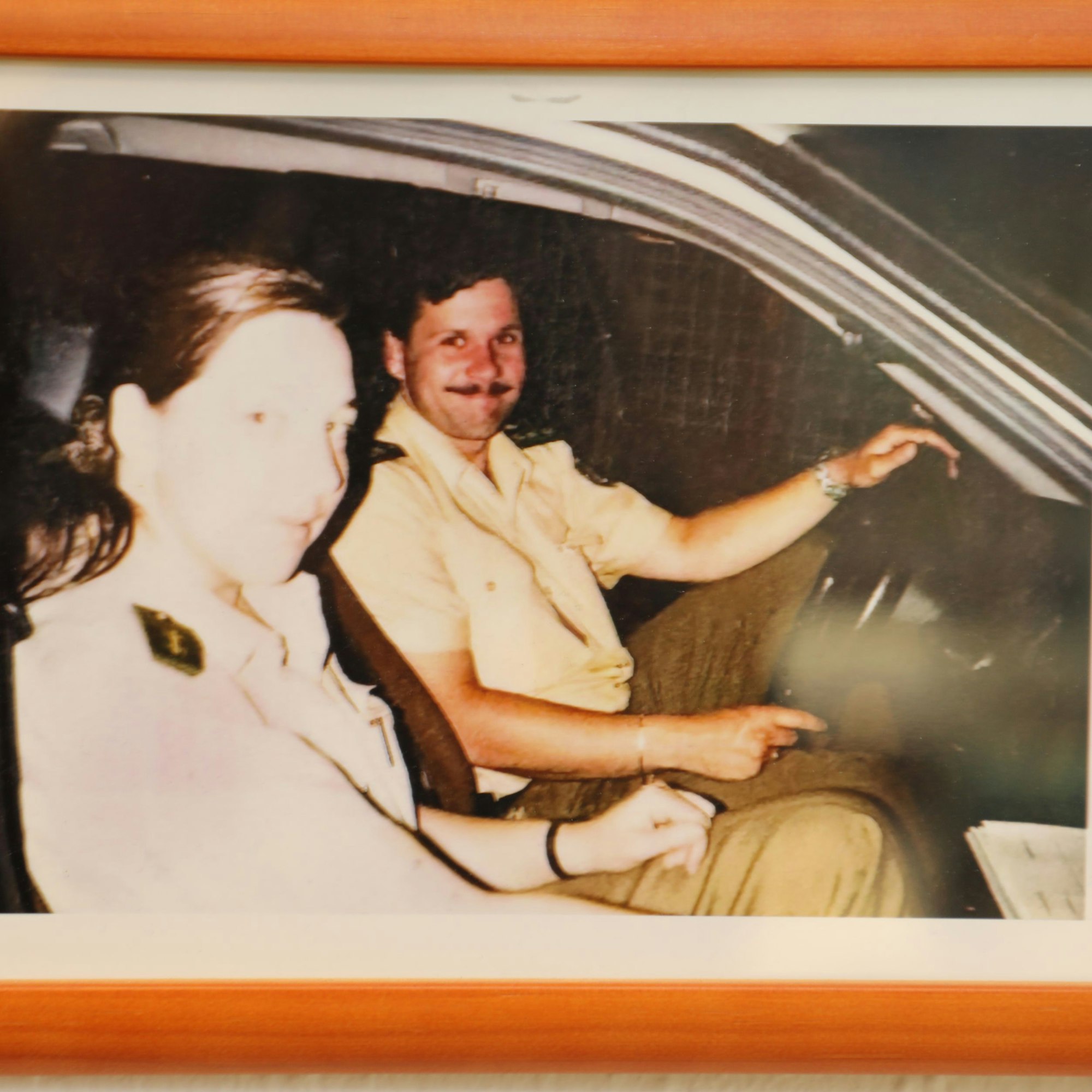 Auf einem Bild in einem Bilderrahmen sind zwei Polizeibeamte in einem Polizeiwage zu sehen.