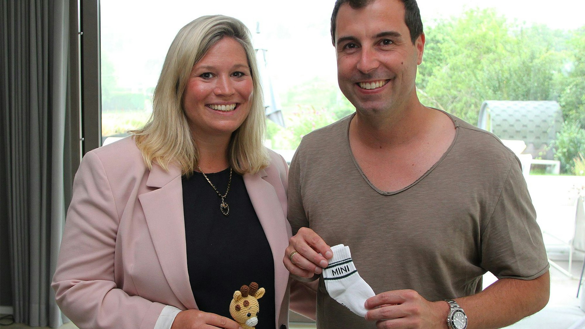 Jennifer Meuren hält ein kleines Spielzeug in der Hand, ihr Ehemann Krishan Babysöckchen. Sie freuen sich auf die Geburt ihres ersten Kindes im Oktober.