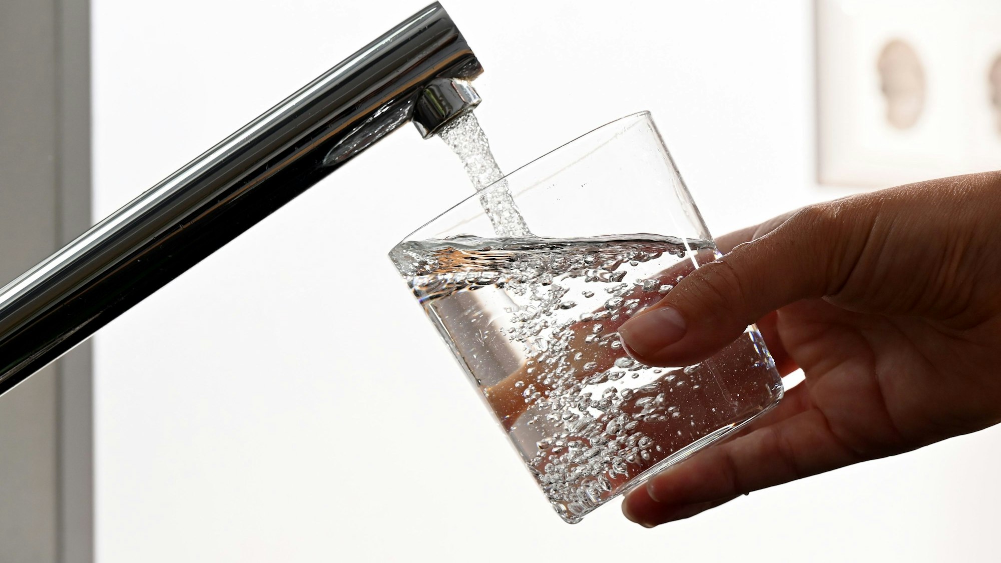 Auf dem Symbolfoto ist eine Hand zu sehen, die ein Wasserglas unter einen laufenden Wasserhahn hält.