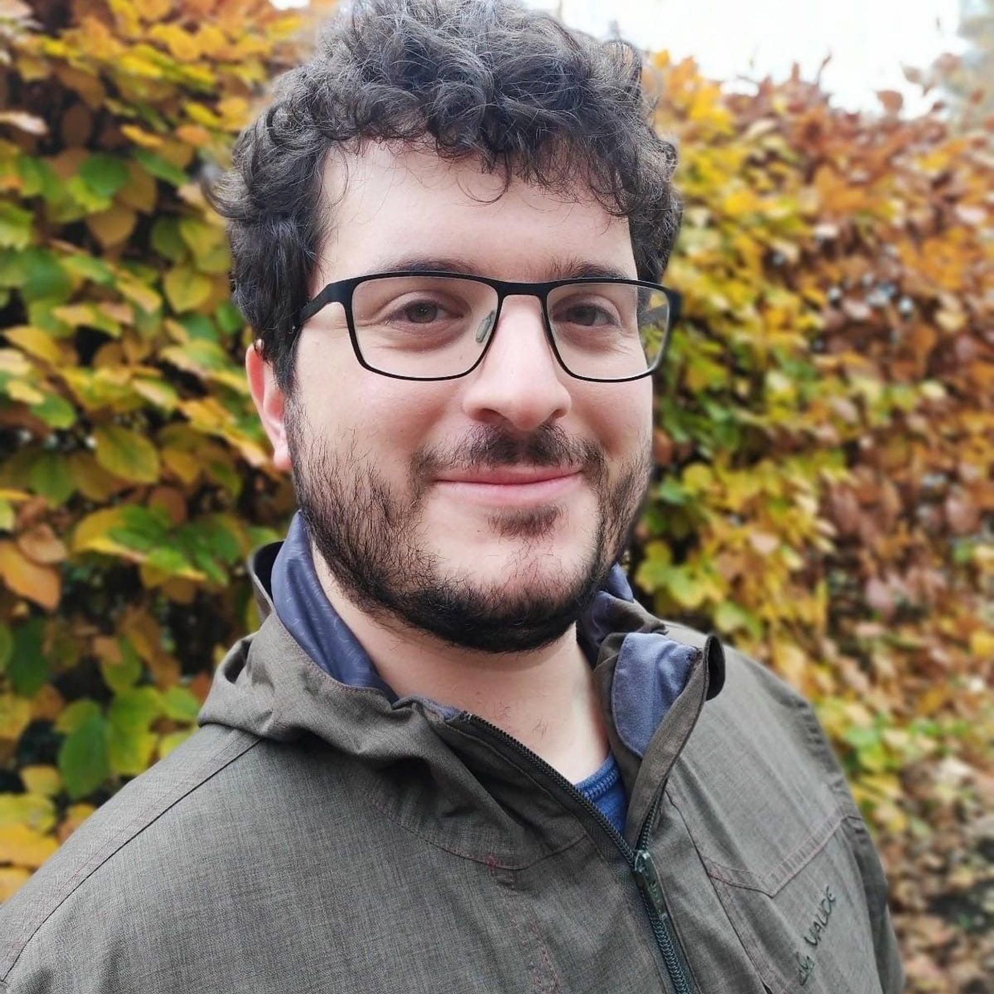 Politologe Jens Wäckerle von der Uni Köln ist im Freien zu sehen, hinter ihm eine herbstlich anmutende Hecke.