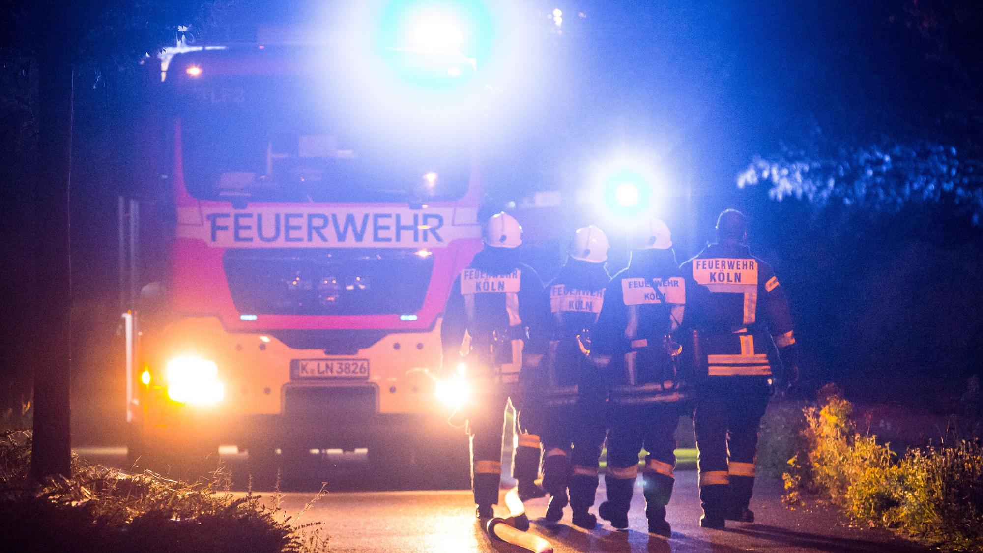 Feuerwehrleute laufen bei Nacht vor einem Einsatzwagen entlang.