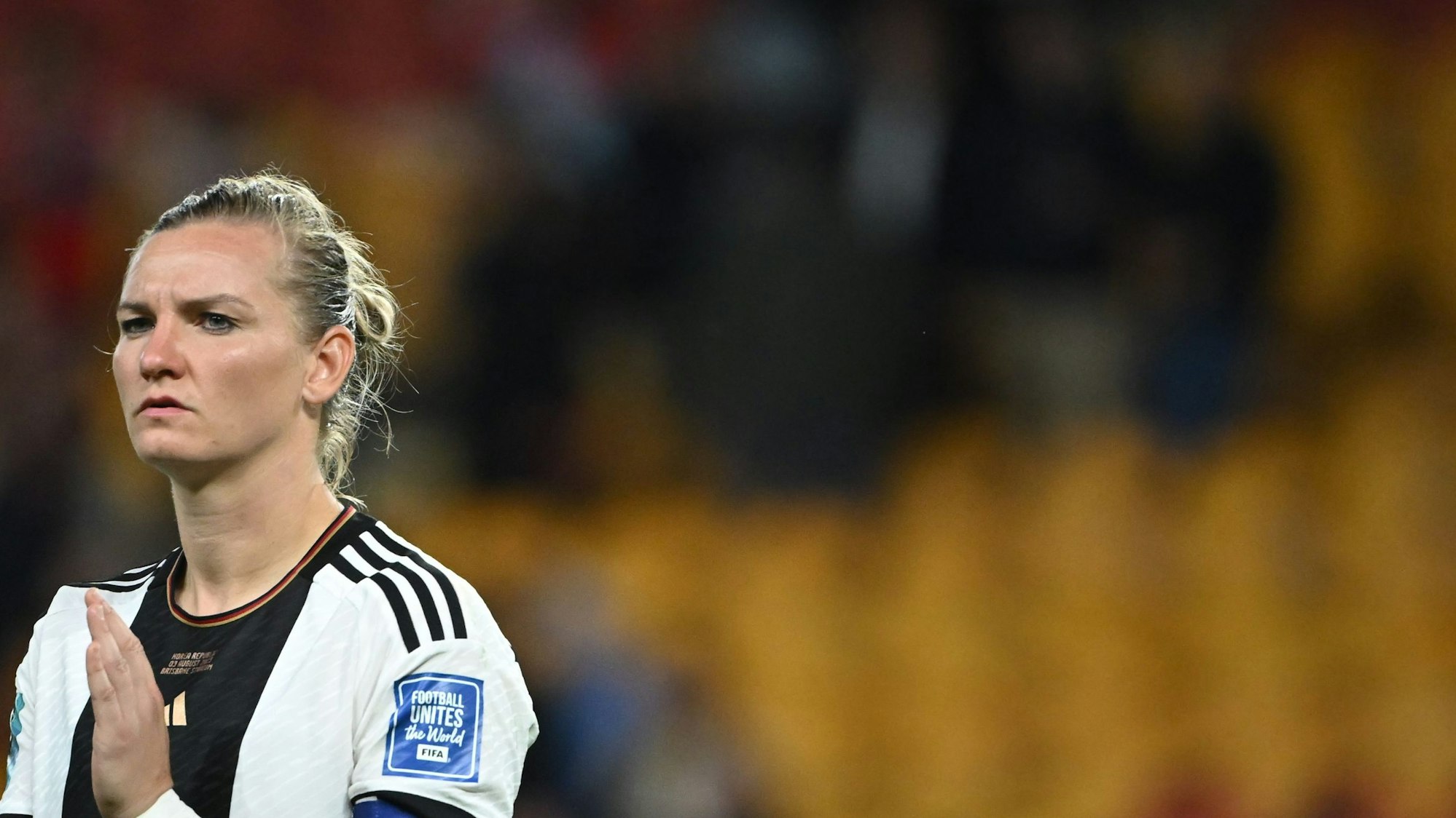 Alexandra Popp steht mit frustriertem Gesichtsausdruck auf dem Spielfeld. Die Tribüne im Hintergrund ist verschwommen.
