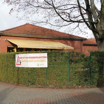 Das Gebäude ragt hinter einer Hecke hervor.