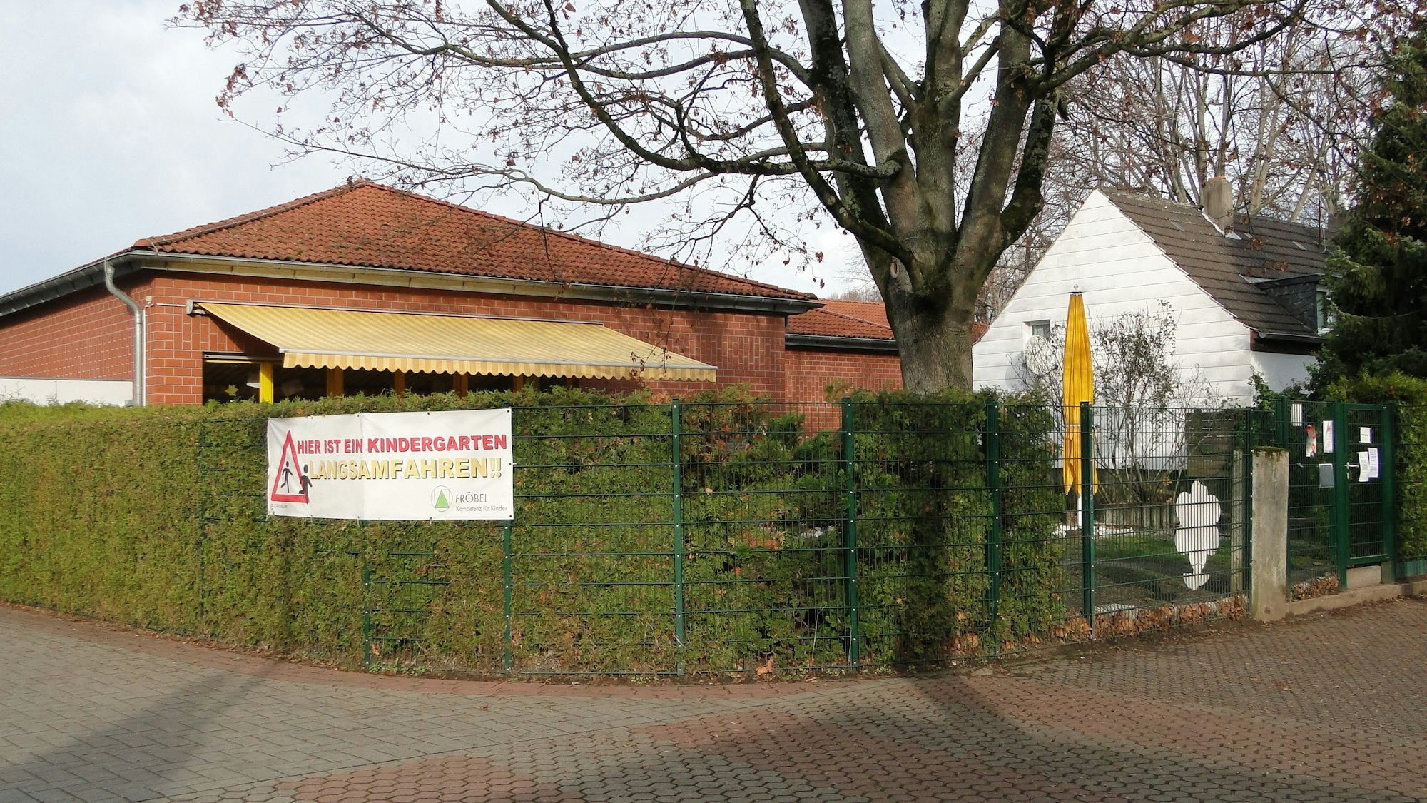 Das Gebäude ragt hinter einer Hecke hervor.