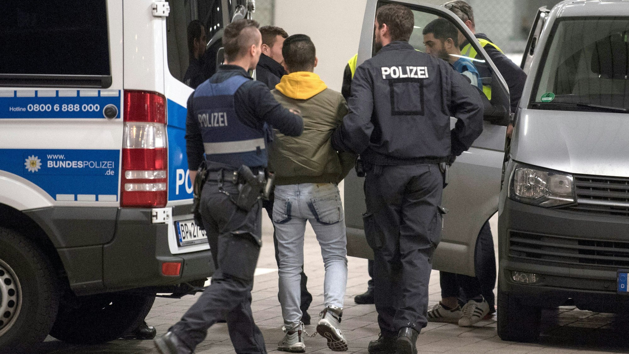 Hand und Fußfesseln trägt ein junger Mann aus Afghanistan, den Polizisten zur Abschiebung zum Flughafen bringen.