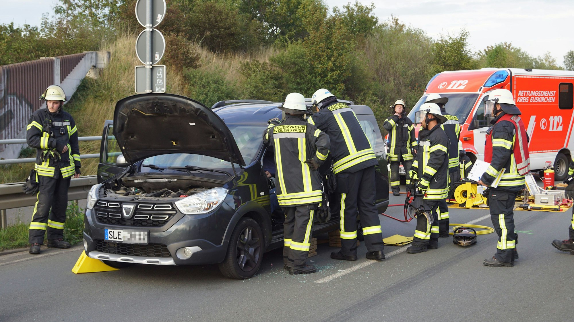 Das Bild zeigt die Feuerwehrleute, wie sie den Autofahrer in seinem Fahrzeug betreuen.