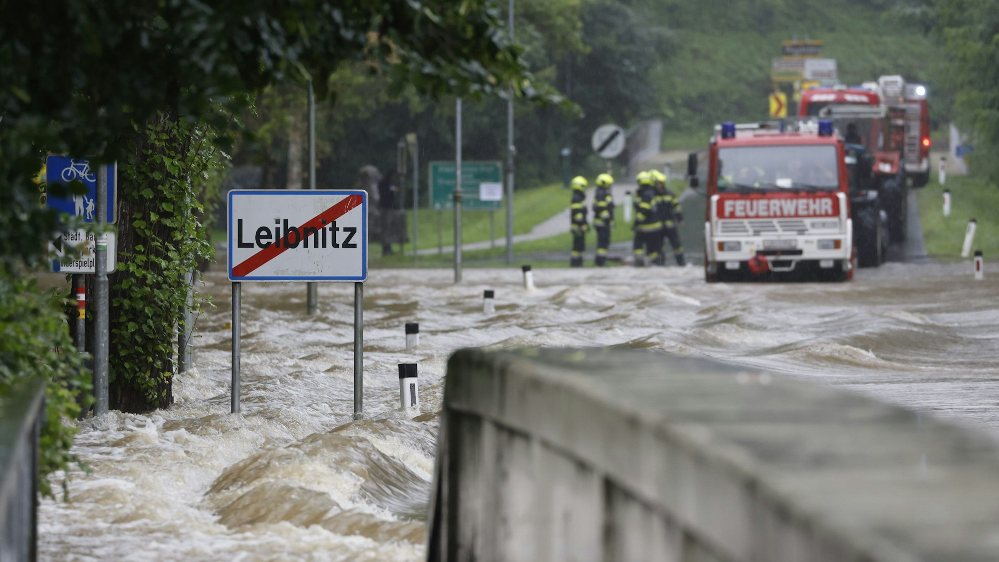 Feuerwehrwagen stehen vor einer überfluteten Brücke über die Sulm am Ortsausgang von Leibnitz in der Steiermark.
