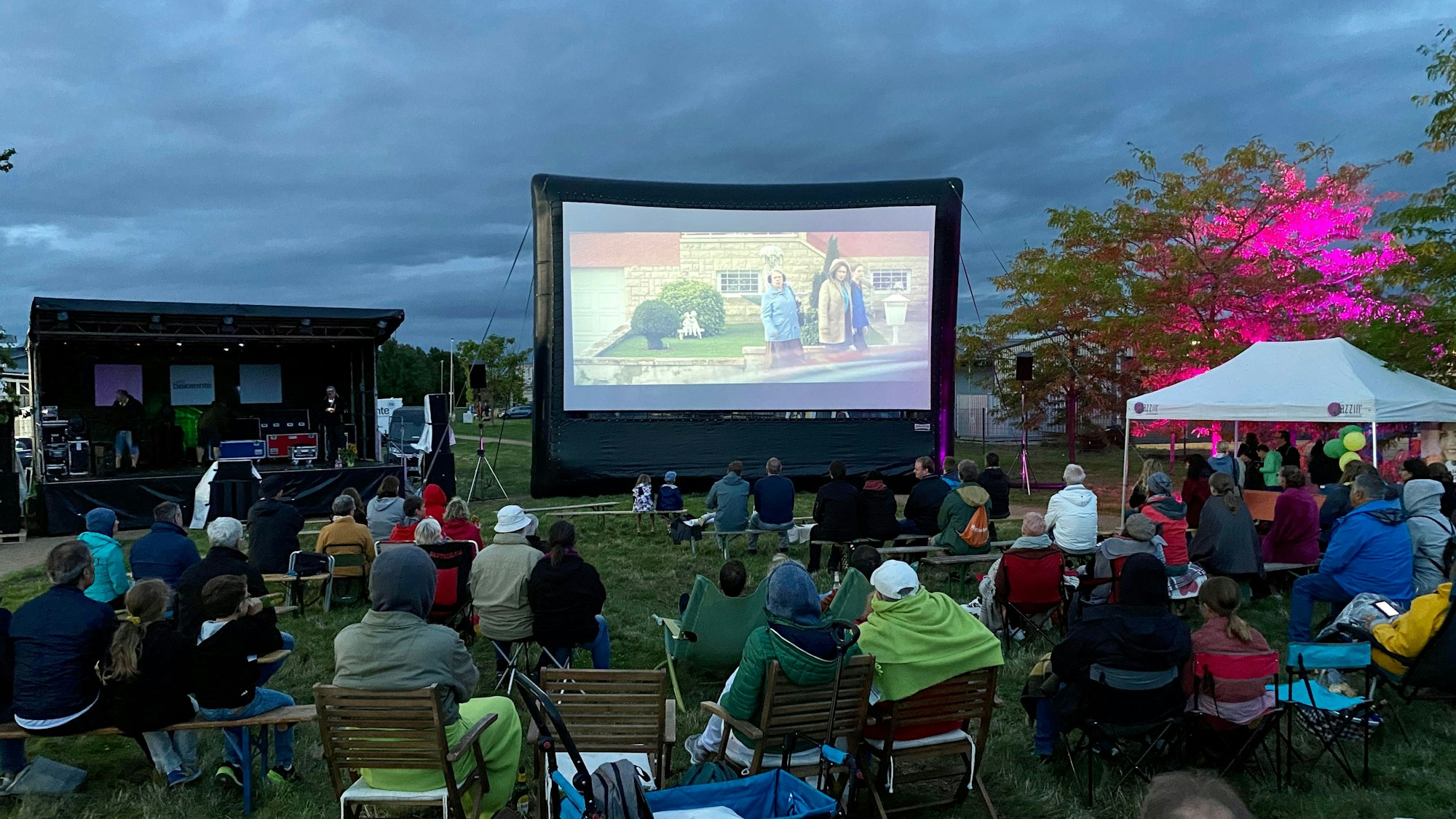 Das Foto zeigt die Zuschauer, die bei hereinbrechender Dunkelheit vor einer großen Leinwand sitzen.