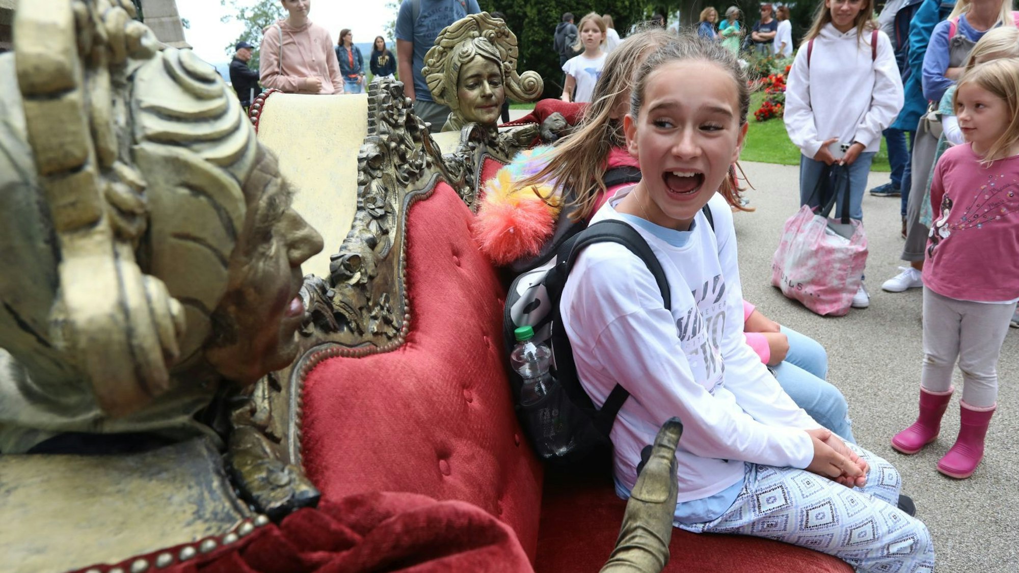 Darsteller, von denen nur die goldenen Köpfe und ein Arm zu sehen sind. stecken in der Rückenlehne eines roten Sofas und sprechen vor allem mit vielen Kindern.