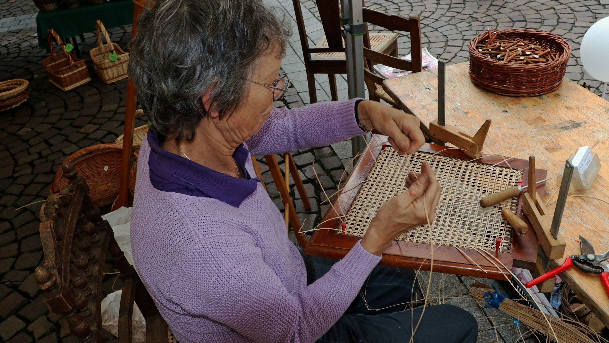 Die Korbmacherin repariert die defekte Rückenlehne eines Stuhls mit Korbgeflecht.